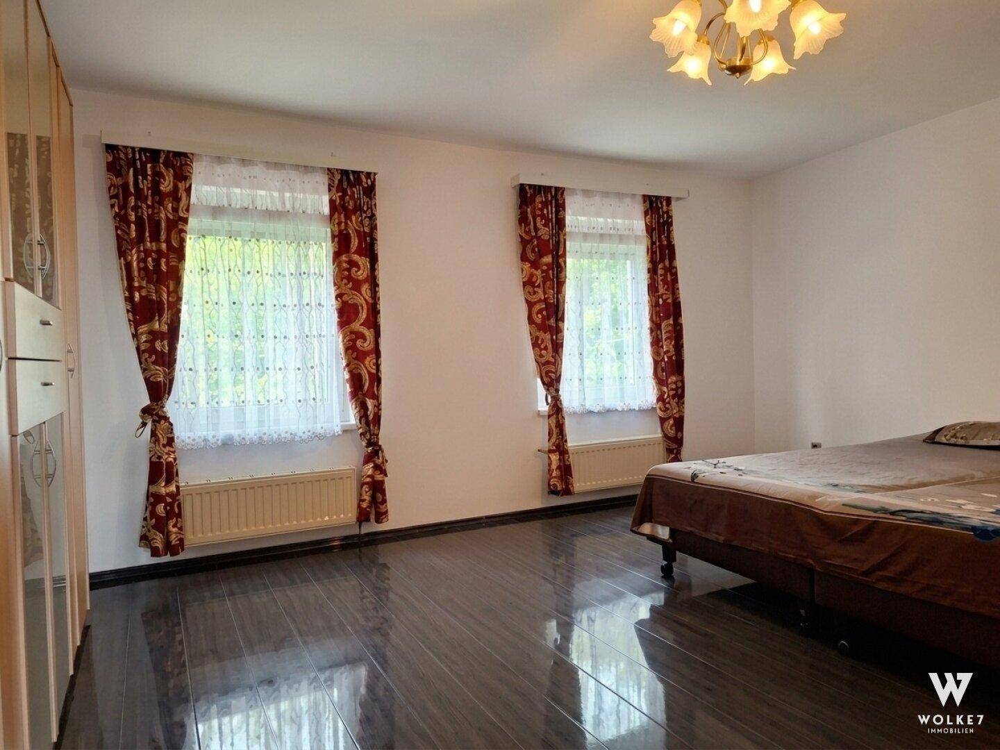 Schlafzimmer mit zwei Fenstern, dunklem Boden und traditionellen Vorhängen.