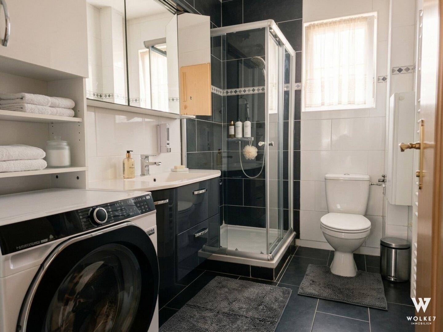 Modernes Badezimmer mit Dusche, Waschmaschine und dunklen Fliesen.