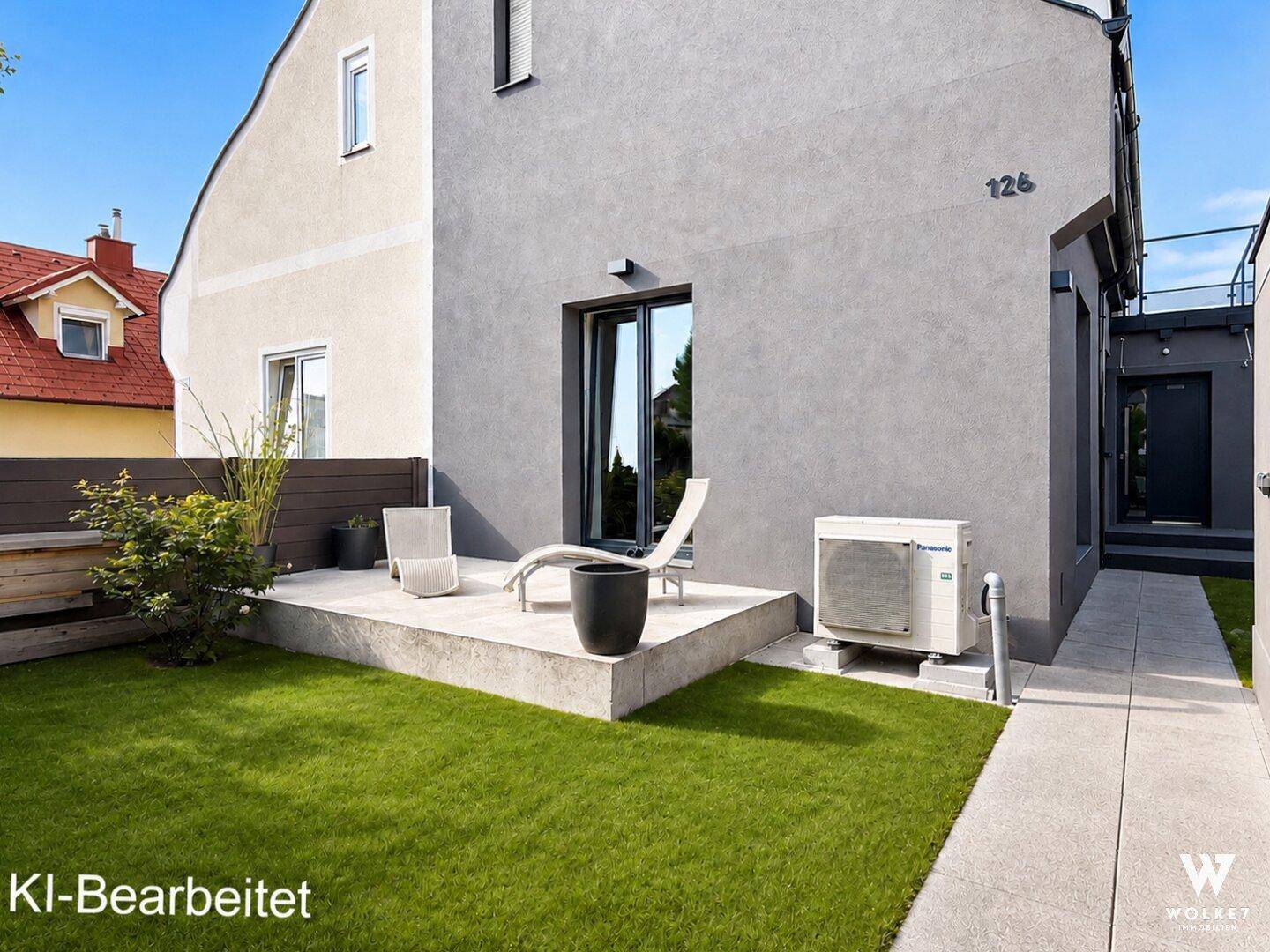 Kleine Terrasse mit Liegestuhl und Rasenfläche neben dem modernen Haus.