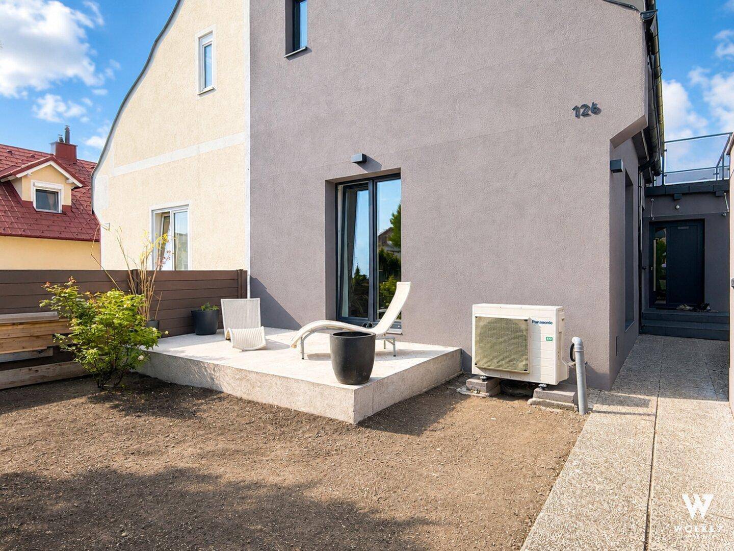 Terrasse mit Liegestuhl und vorbereiteter Gartenfläche neben dem modernen Haus.