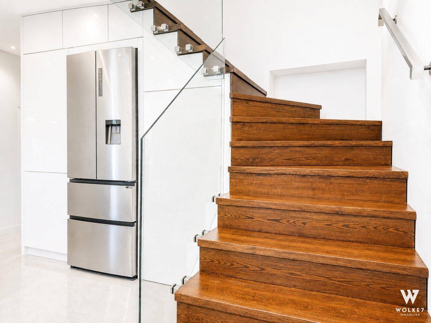 Moderne Holztreppe mit Glasgeländer und integriertem Kühlschrank in weißer Küchenzeile.