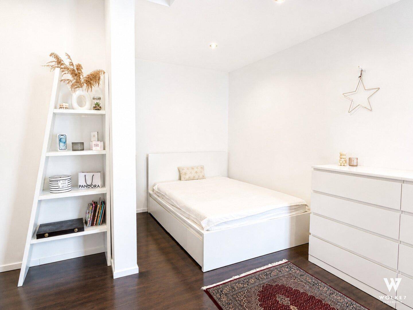 Gemütliches Schlafzimmer mit Einzelbett, weißem Regal und dunklem Holzboden.