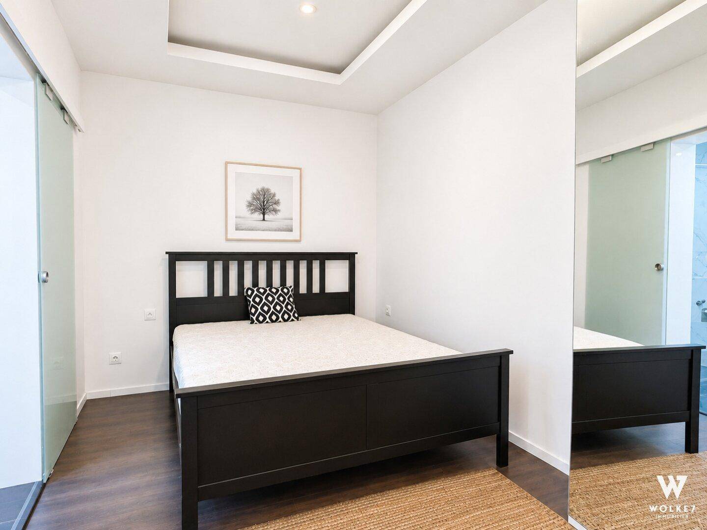 Modernes Schlafzimmer mit dunklem Bett, Holzboden und Schiebetür zum Bad.