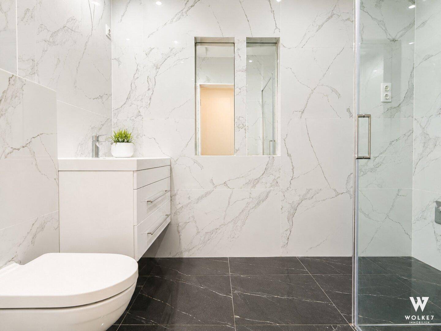 Elegantes Badezimmer mit Marmorfliesen, wandhängendem WC und begehbarer Dusche.