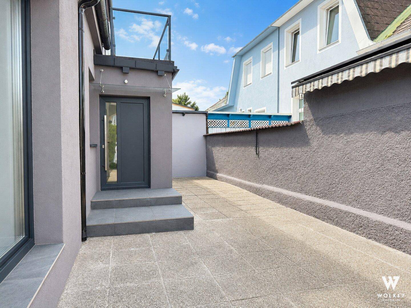 Gepflasterter Außenbereich neben dem Haus mit Zugang zu einer oberen Terrasse.