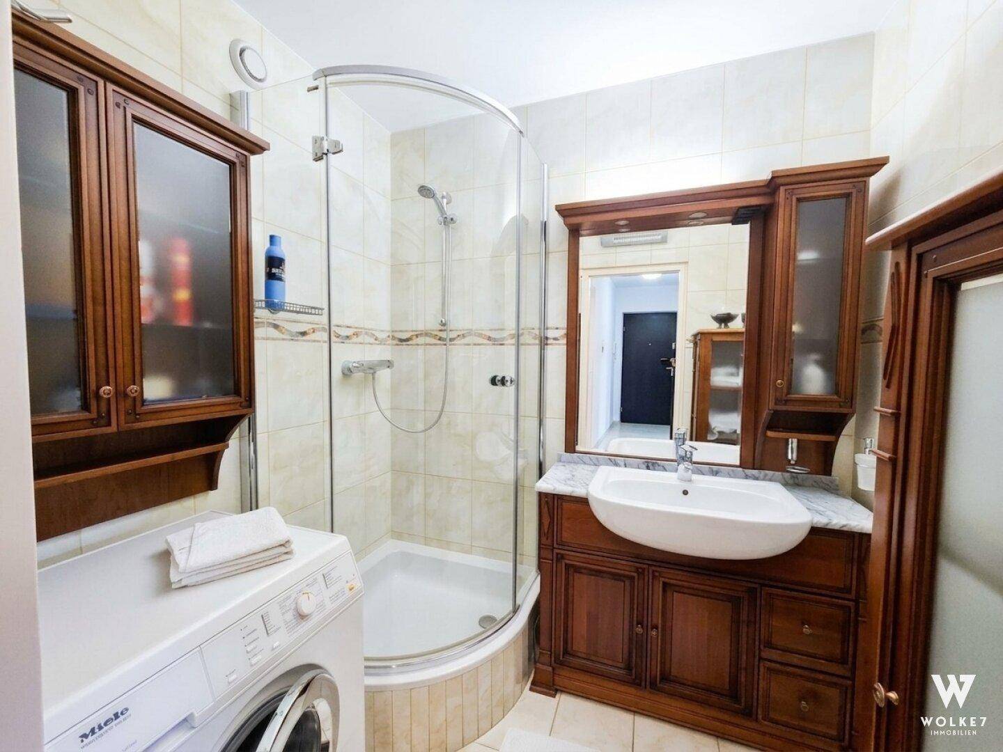 Badezimmer mit Eckdusche, Waschtisch mit Marmorplatte und integrierter Waschmaschine.