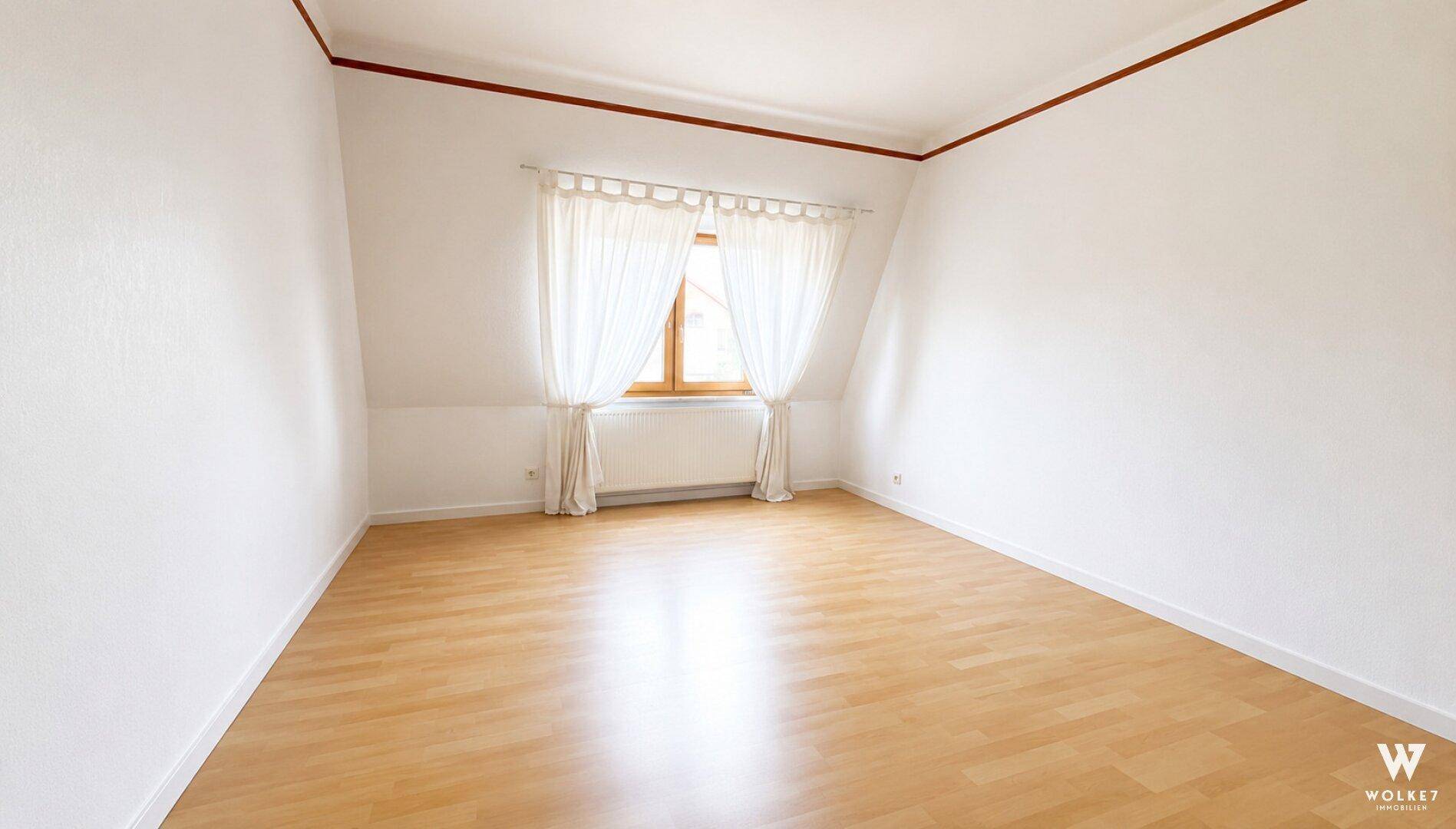 Unmöbliertes Schlafzimmer im Dachgeschoss mit schrägen Wänden, Laminatboden und einem Fenster.