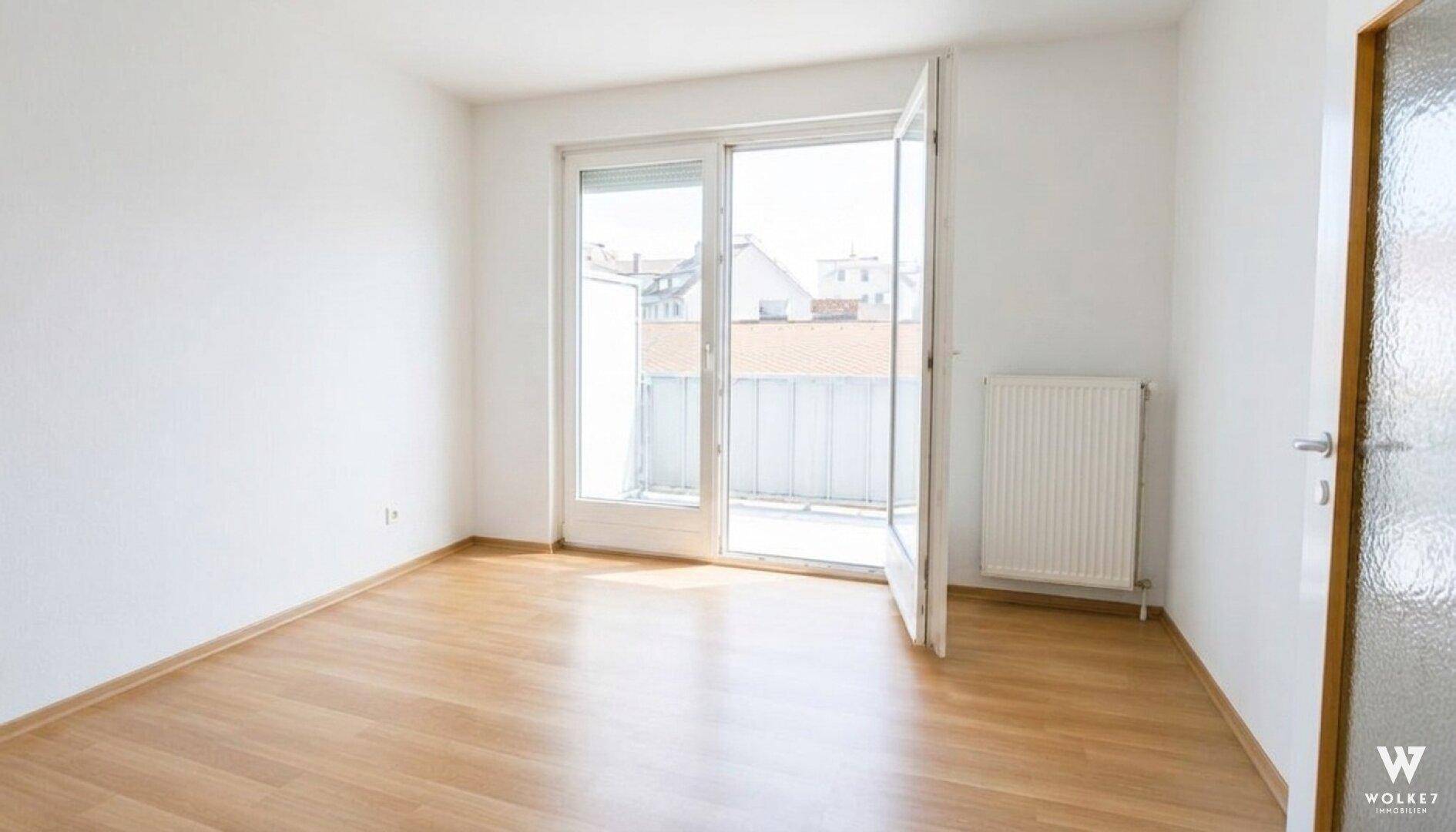 Heller, unmöblierter Raum mit Laminatboden und einer großen Balkontür, die viel Licht hereinlässt.