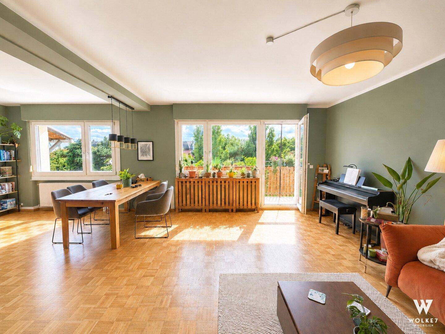 Heller, offener Wohn- und Essbereich mit Parkettboden, grünen Wänden und Zugang zum Balkon.