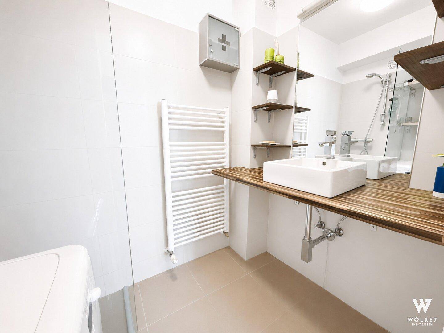 Modernes Badezimmer mit Waschbecken, Holzablage und beheiztem Handtuchhalter.