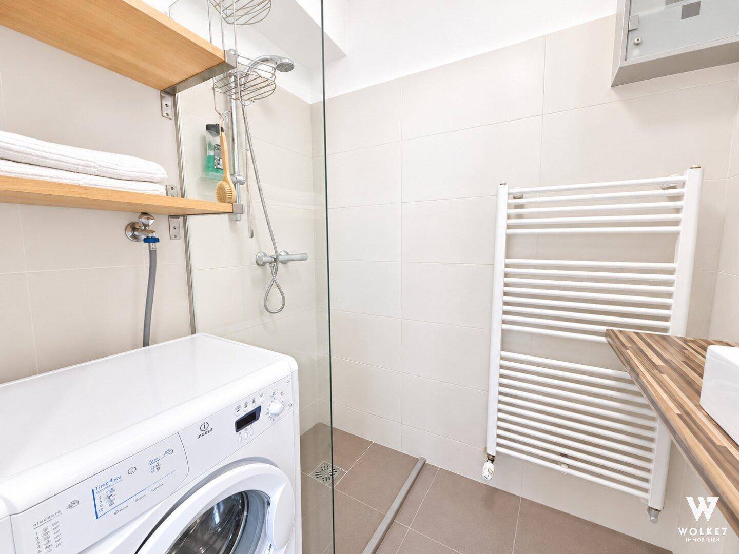 Helles Badezimmer mit Dusche, Waschmaschine und beheiztem Handtuchhalter.