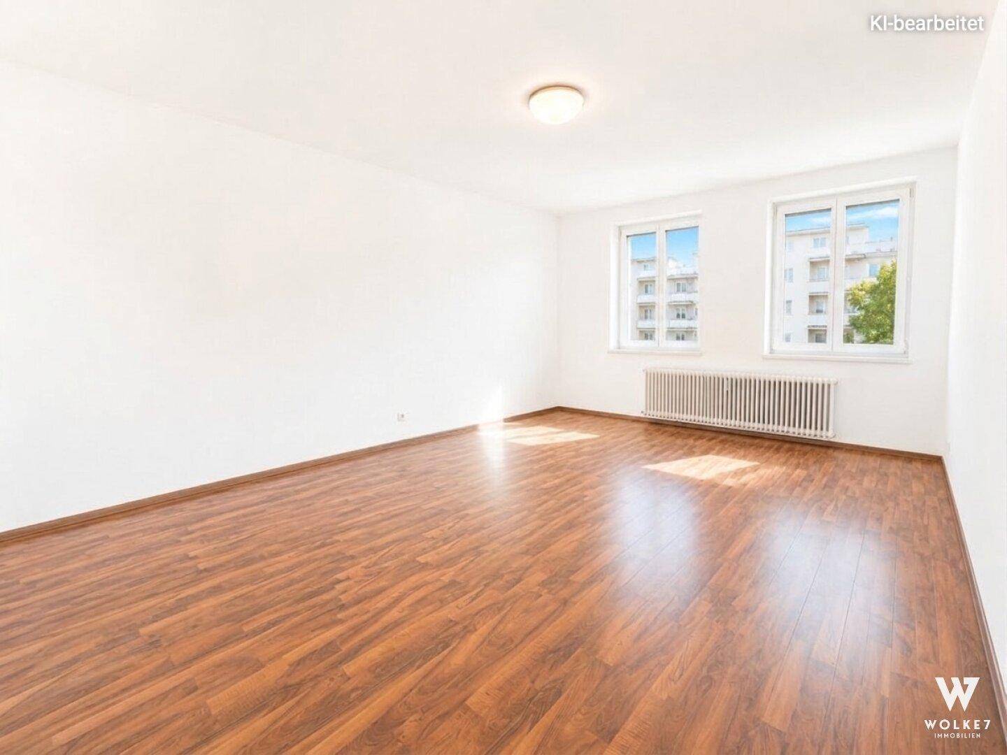 Geräumiges, leeres Wohnzimmer mit Laminatboden und großen Fenstern, die viel Tageslicht hereinlassen.