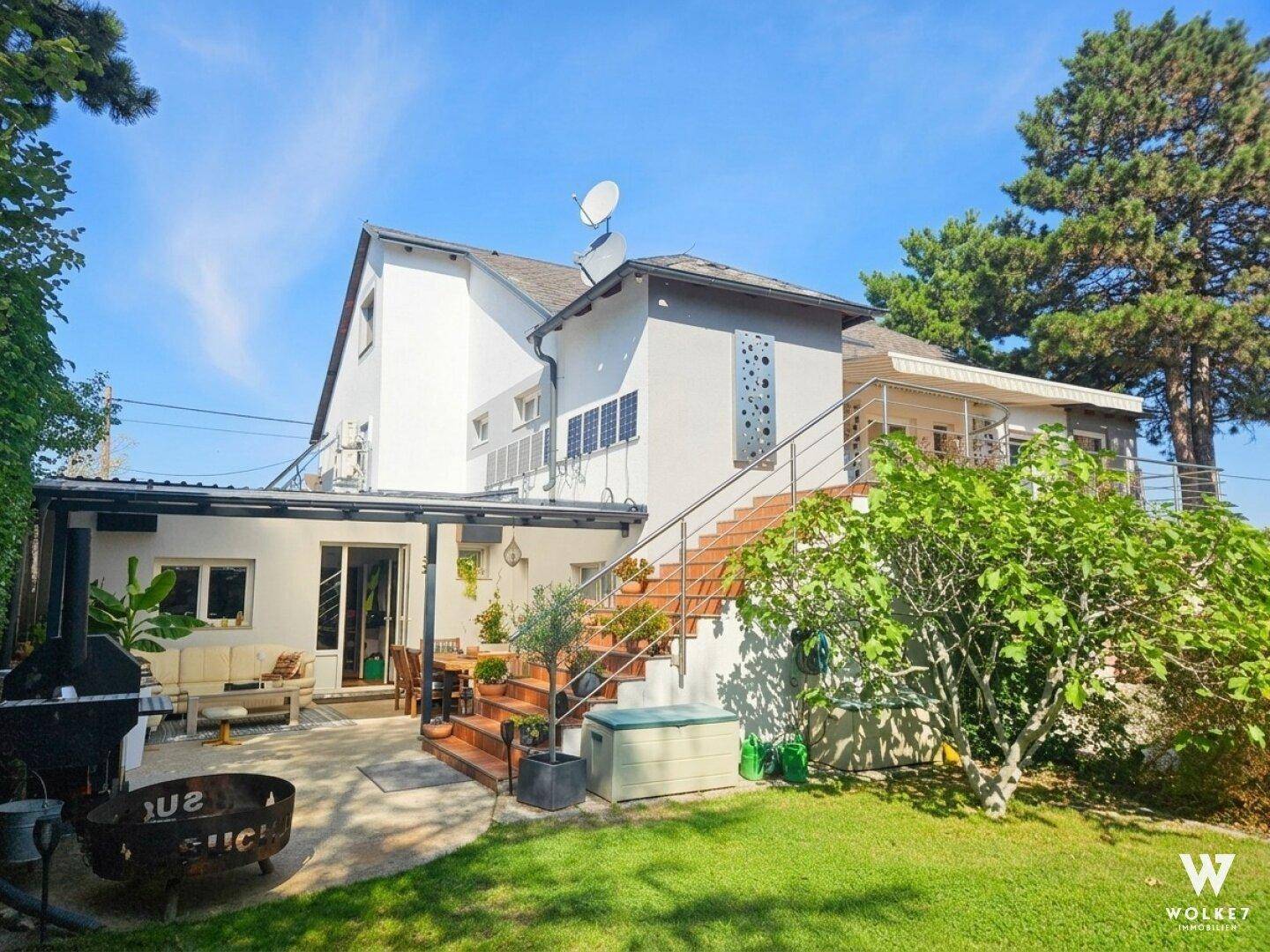 Rückseite des Hauses mit großer Terrasse, Außentreppe und Grillbereich im Garten.