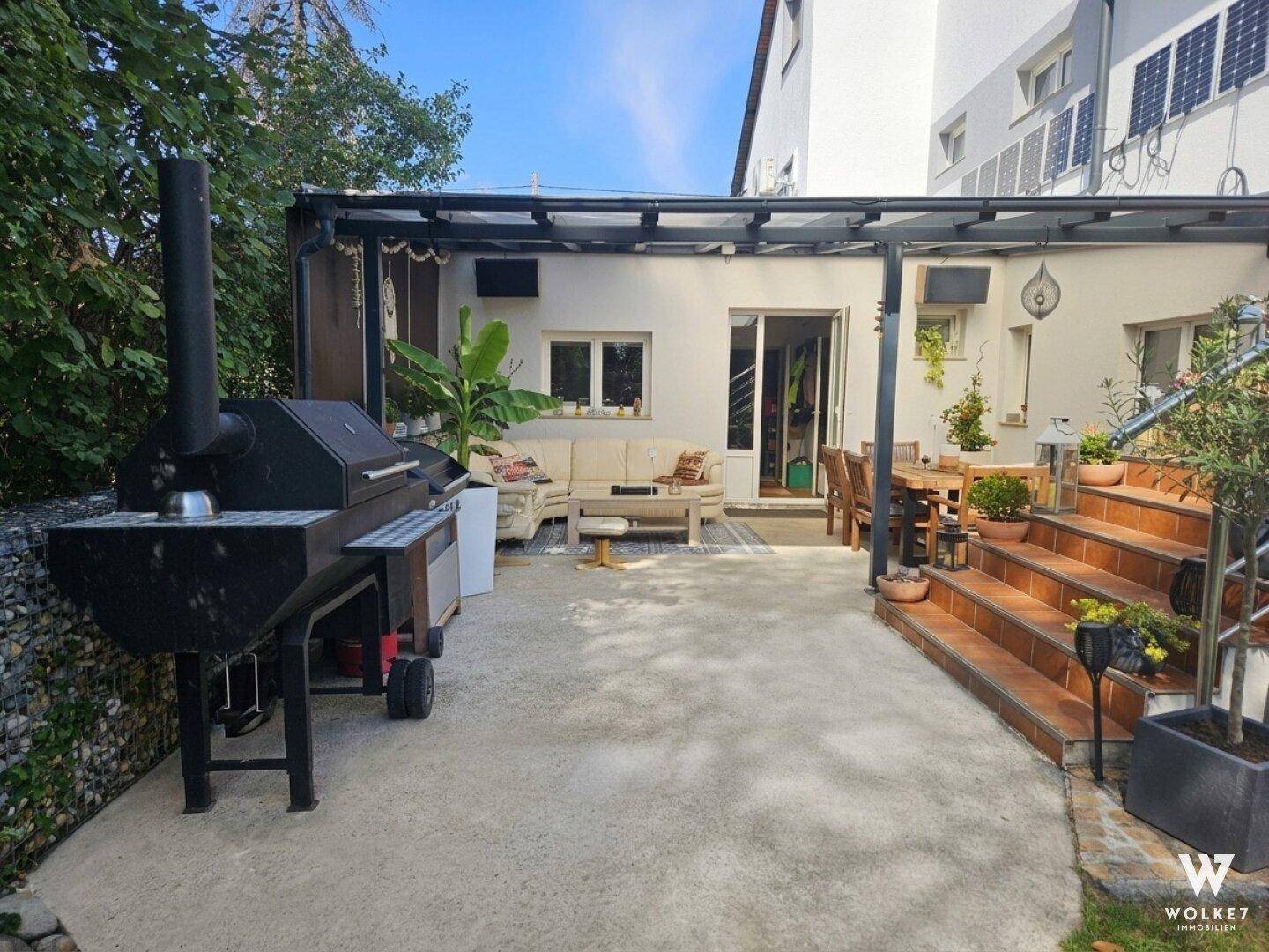 Überdachte Terrasse mit großem Grill und gemütlicher Sitzecke, ideal für Mahlzeiten im Freien.