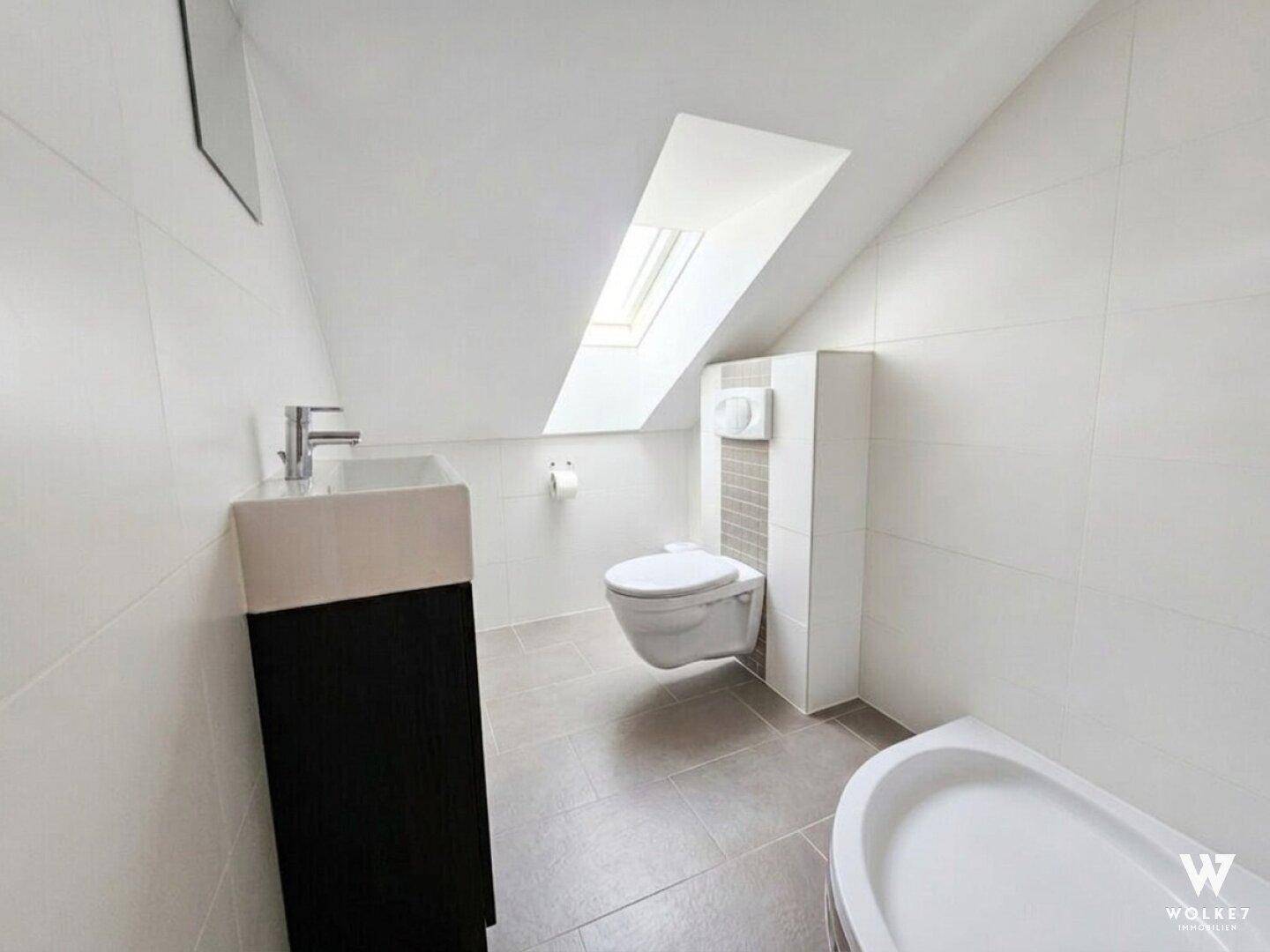 Helles Gäste-WC mit Wand-WC, kleinem Waschbecken und Dachfenster.