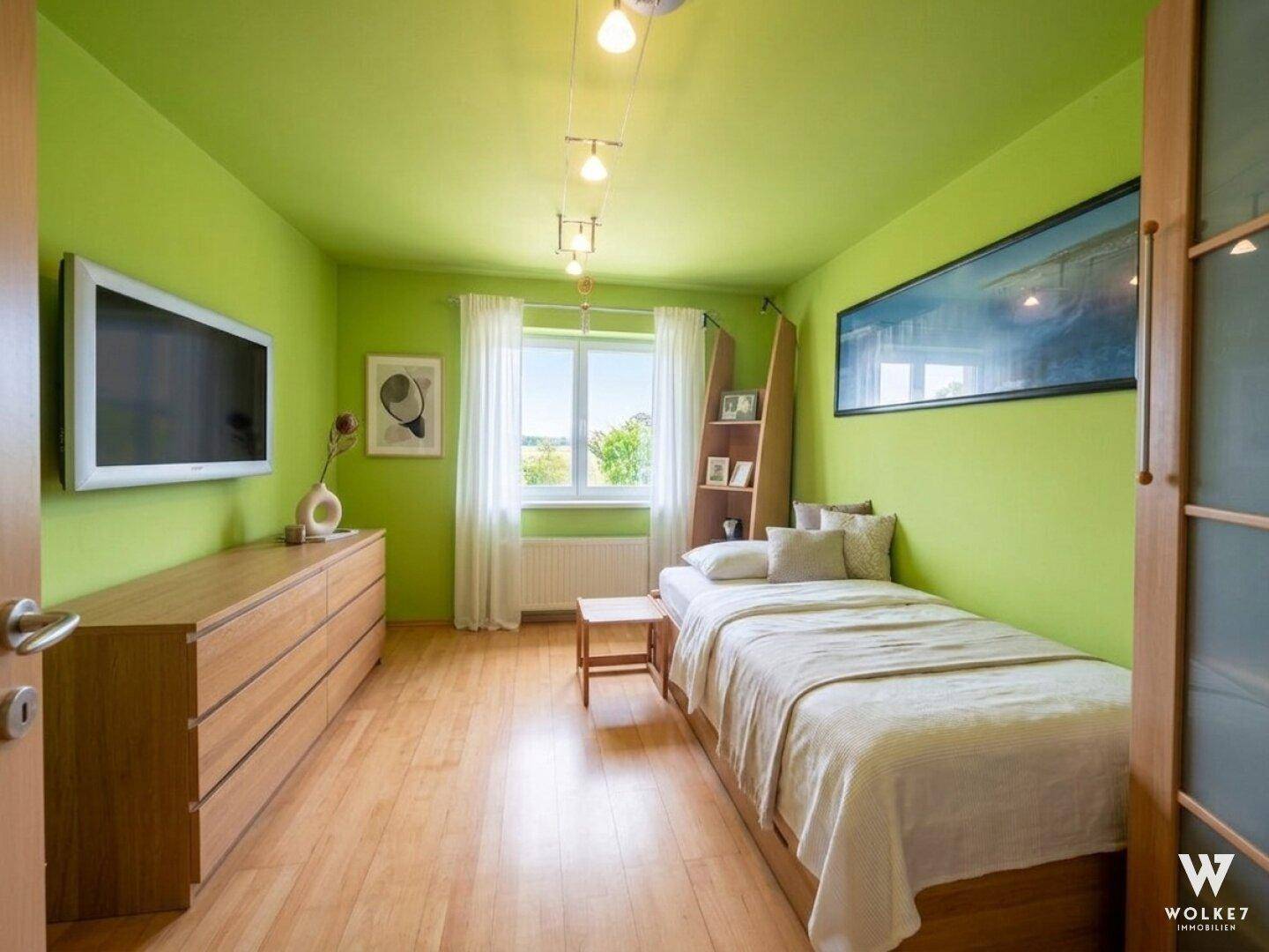 Helles Schlafzimmer mit grünen Wänden, Holzboden und Einzelbett, mit Blick ins Grüne.
