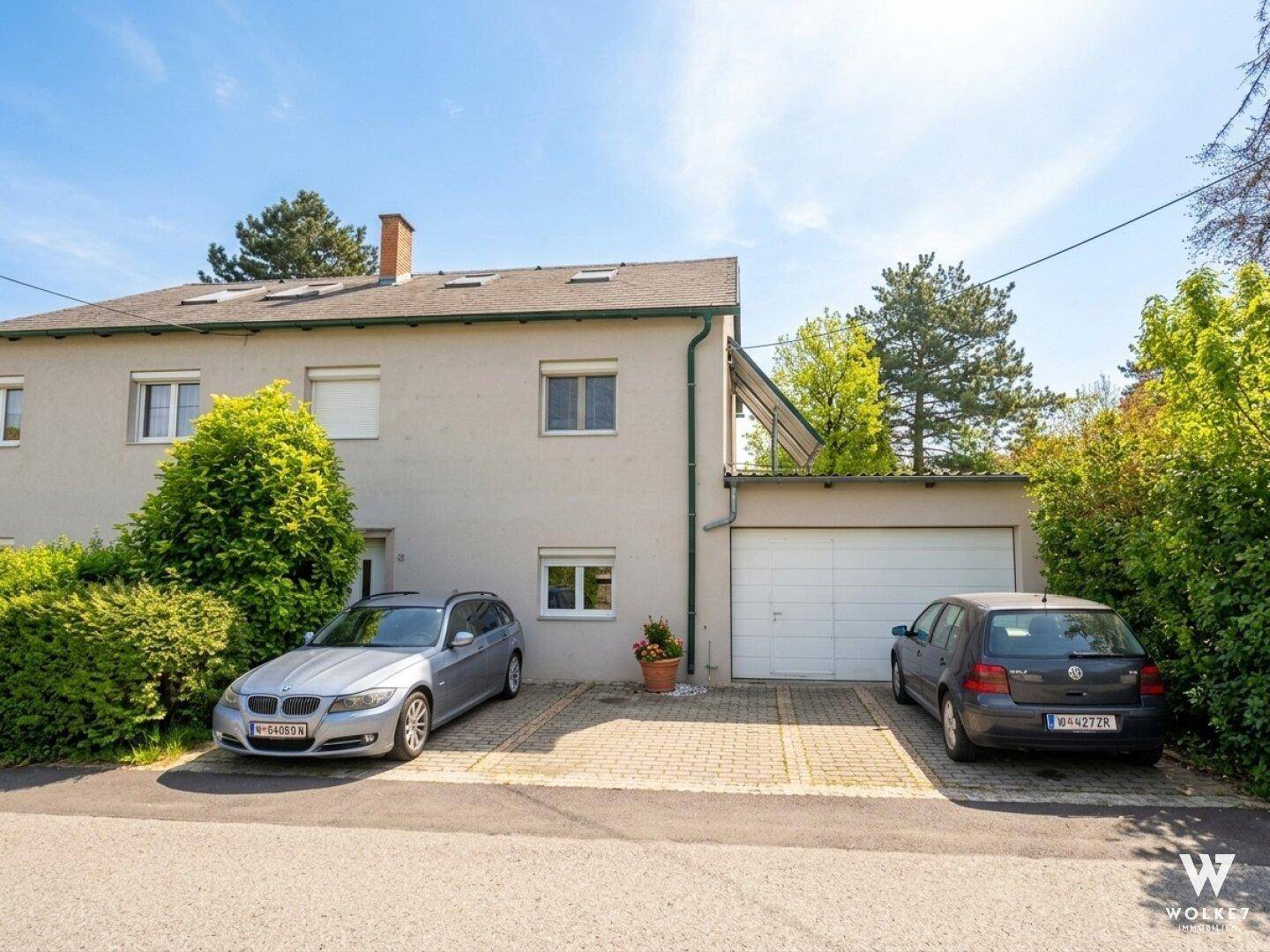 Vorderansicht des Hauses mit Garage, gepflasterten Parkplätzen und grüner Bepflanzung.