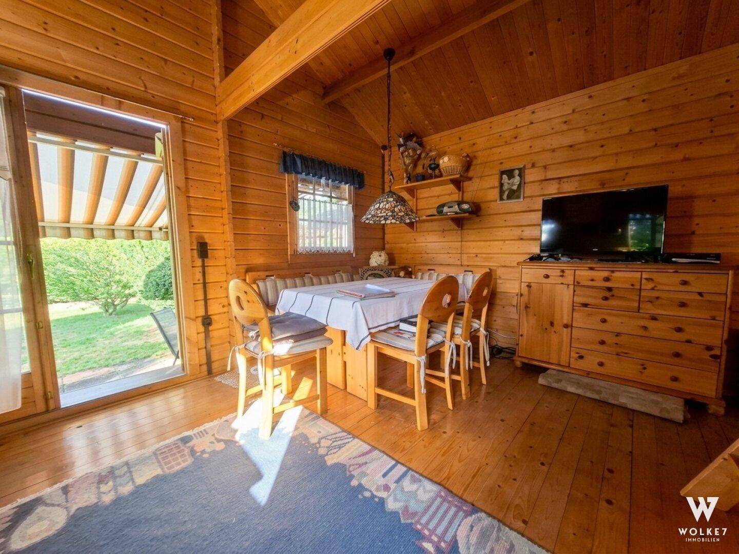 Heller Essbereich in der Holzhütte mit Holztisch, Eckbank und direktem Zugang zum grünen Garten.