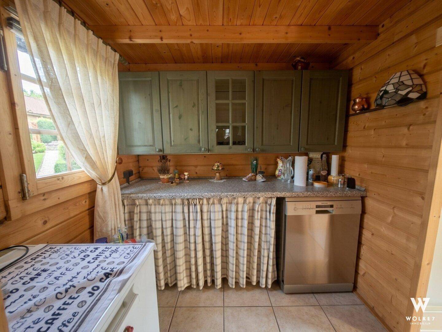 Kleine, funktionale Küche in der Holzhütte mit grünen Schränken, Spülmaschine und Fliesenboden.