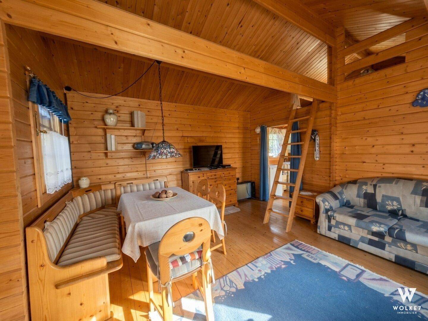 Gemütlicher Wohn-Essbereich in einer Holzhütte mit Eckbank, Sofa und einer Leiter zum Schlafbereich.