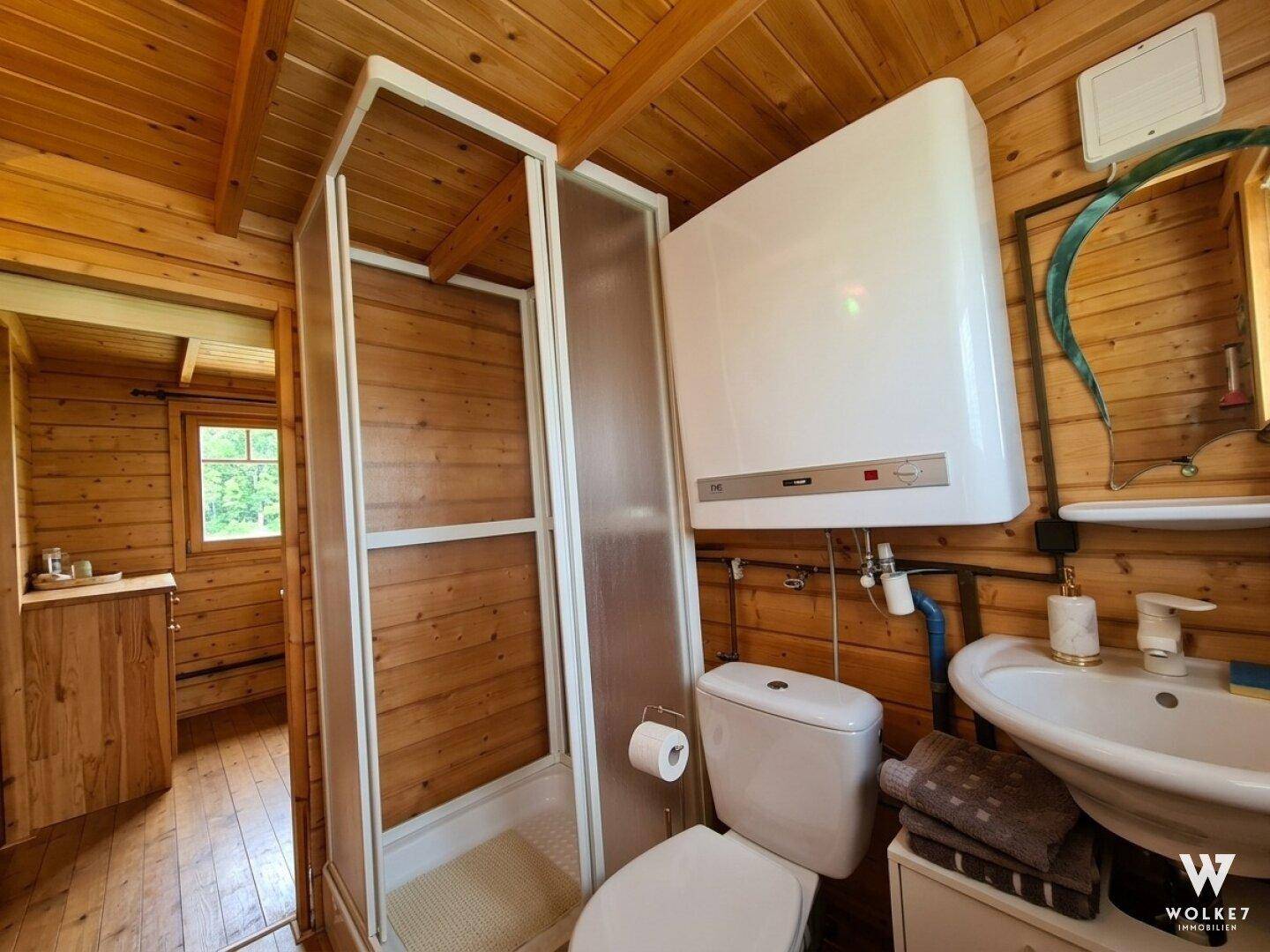 Einfaches Badezimmer in der Holzhütte mit Duschkabine, WC, Waschbecken und Holzvertäfelung an den Wänden.