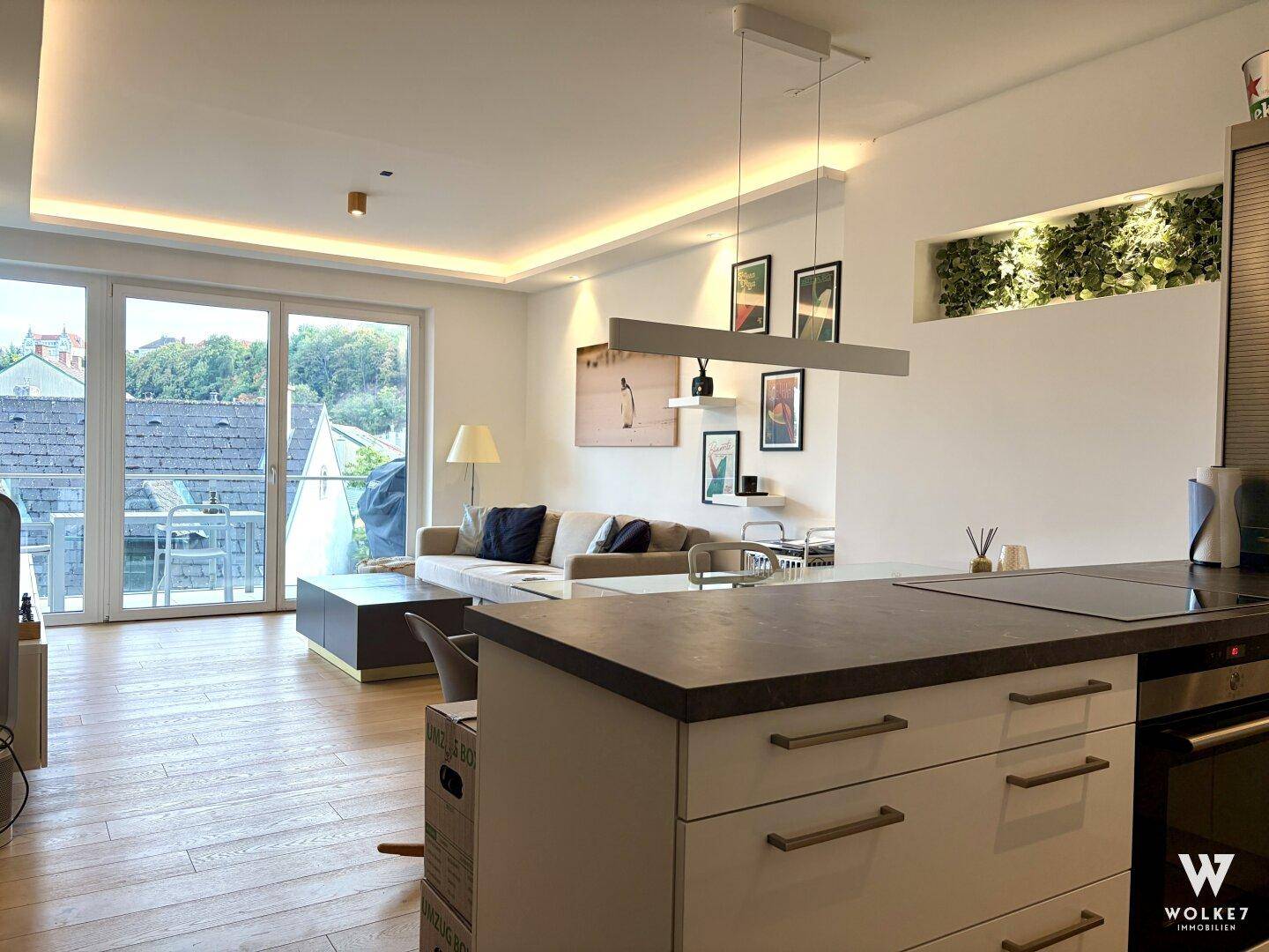Lichtdurchfluteter Wohnbereich mit Zugang zum Balkon, offener Küche und modernem Design.