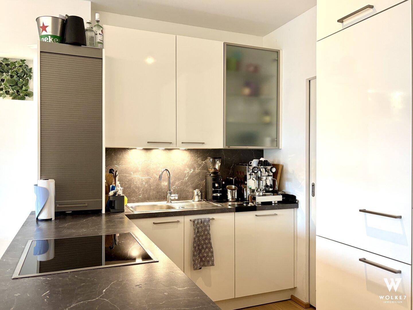 Moderne Einbauküche mit dunkler Arbeitsplatte, Induktionskochfeld und weißen Hochglanzfronten.