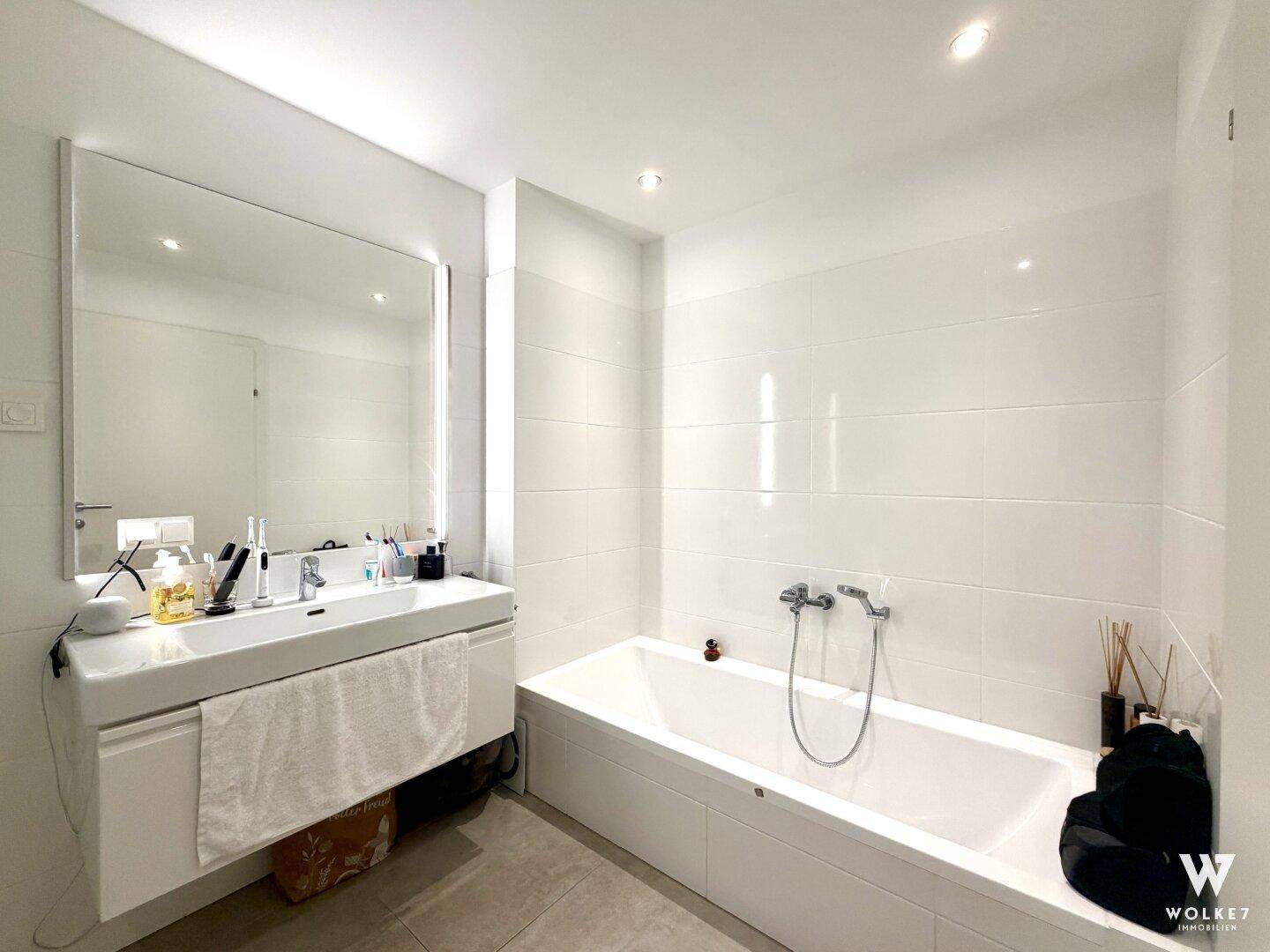 Modernes Badezimmer mit Badewanne, schwebendem Waschtisch und großen weißen Wandfliesen.