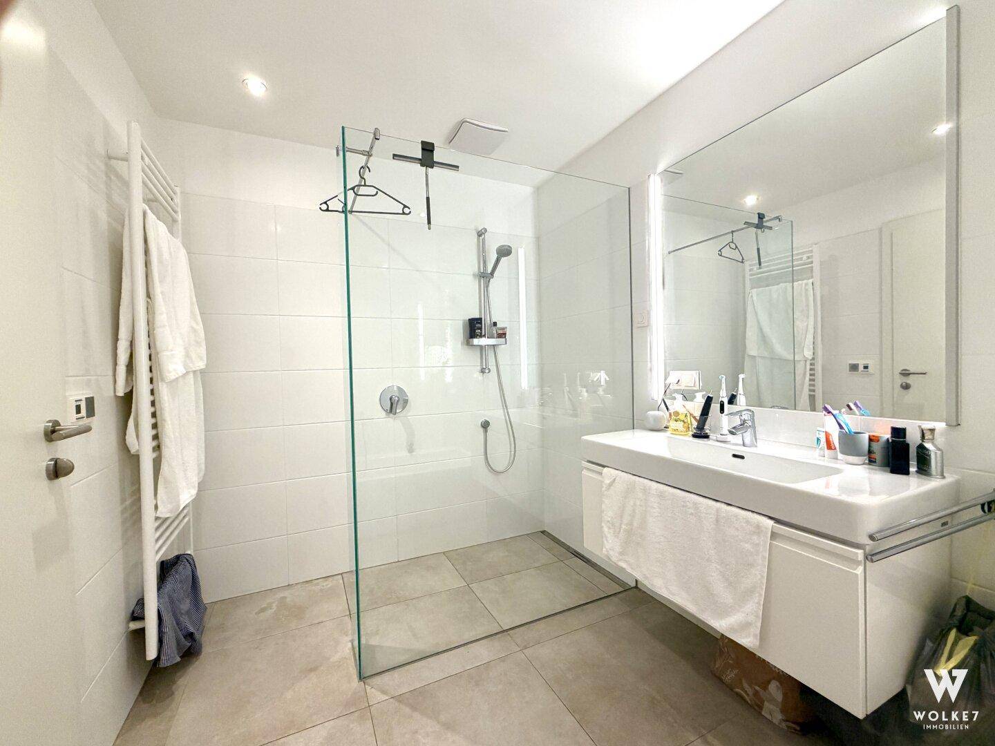 Helles Badezimmer mit ebenerdiger Dusche, großem Spiegel und modernem Waschtisch.