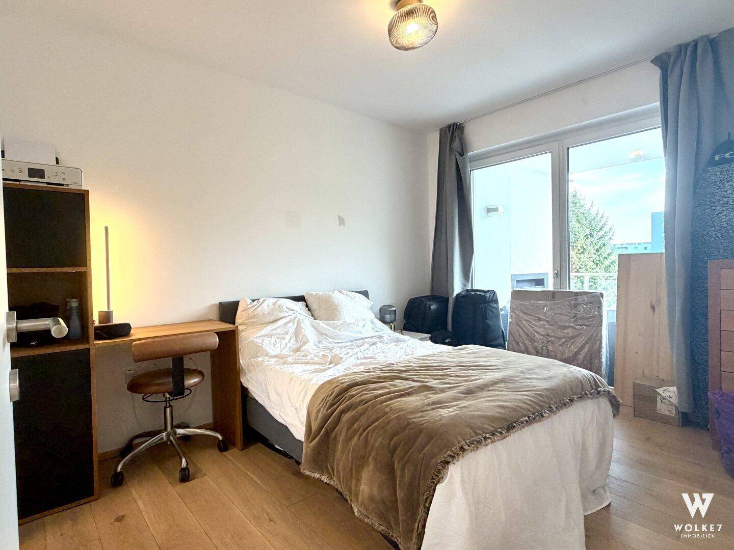 Schlafzimmer mit Holzboden, großem Fenster und Zugang zu einem Außenbereich.