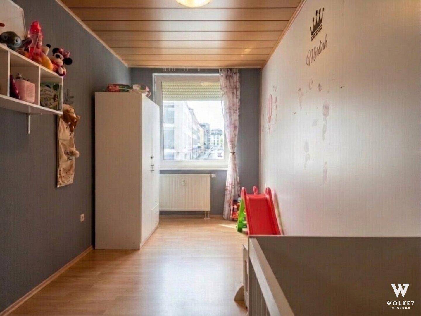 Kinderzimmer mit Holzboden, weißem Kleiderschrank und Spielgeräten.