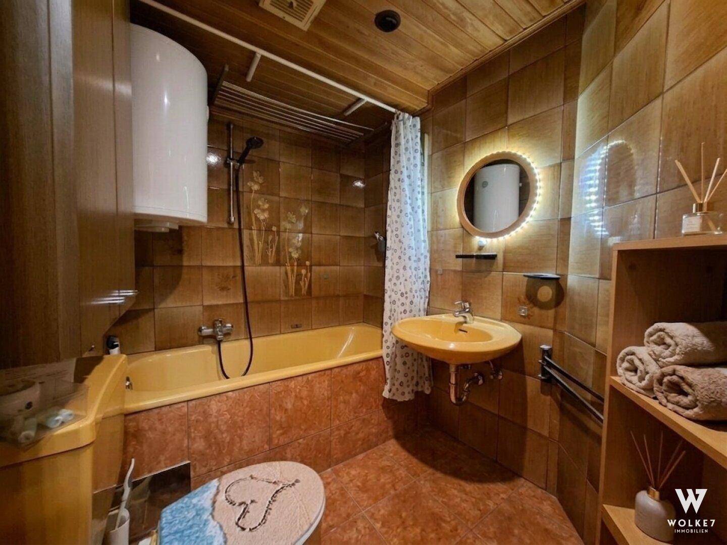 Badezimmer mit gelber Badewanne, Waschbecken und braunen Fliesen.