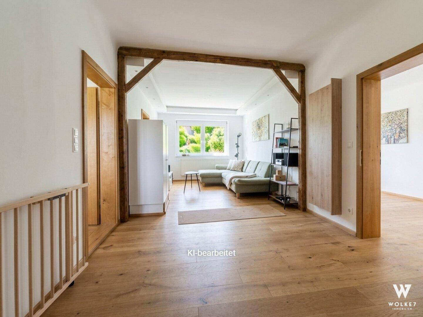 Helles Wohnzimmer mit Holzboden, bequemer Couch und rustikalen Holzbalken als Raumteiler.