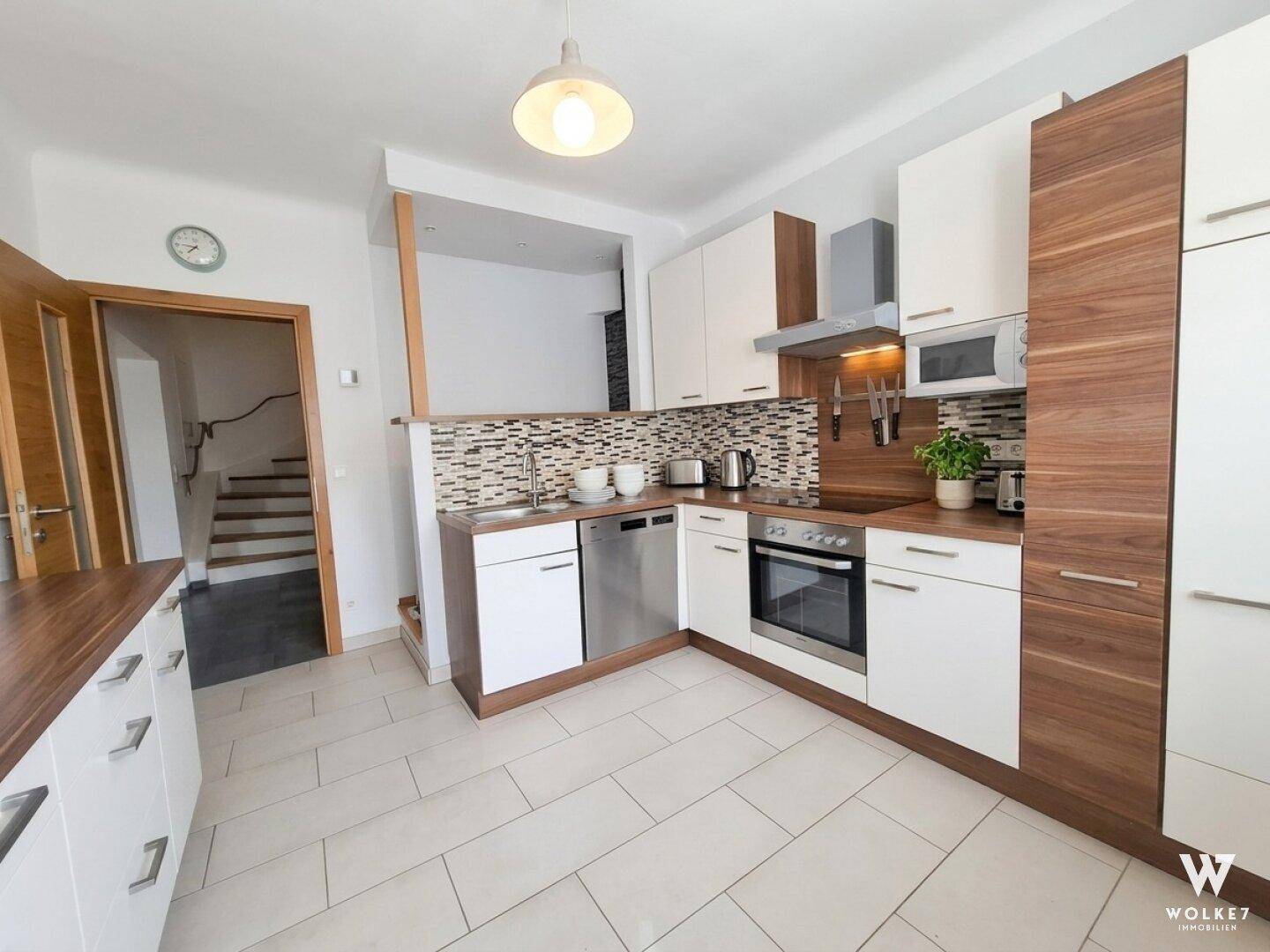 Moderne Küche mit weißen und holzfarbenen Schränken, Einbaugeräten und Fliesenboden.