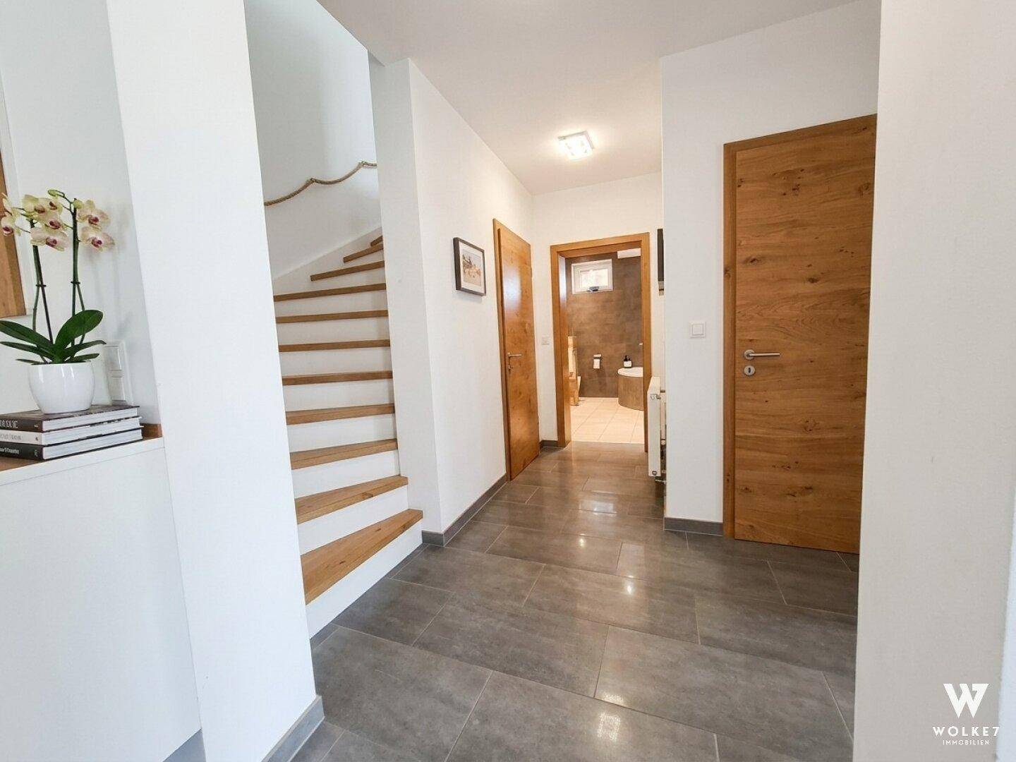 Heller Flur mit grauen Fliesen, Holztreppe und Zugang zu weiteren Räumen.