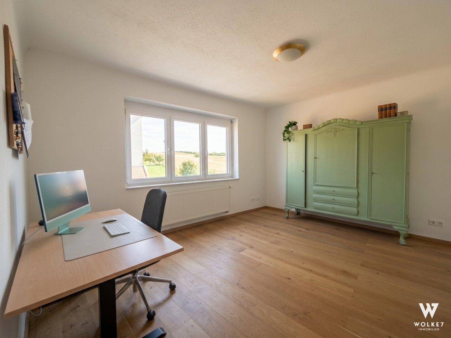 Helles Arbeitszimmer mit Holzboden, Schreibtisch und einem auffälligen grünen Kleiderschrank.