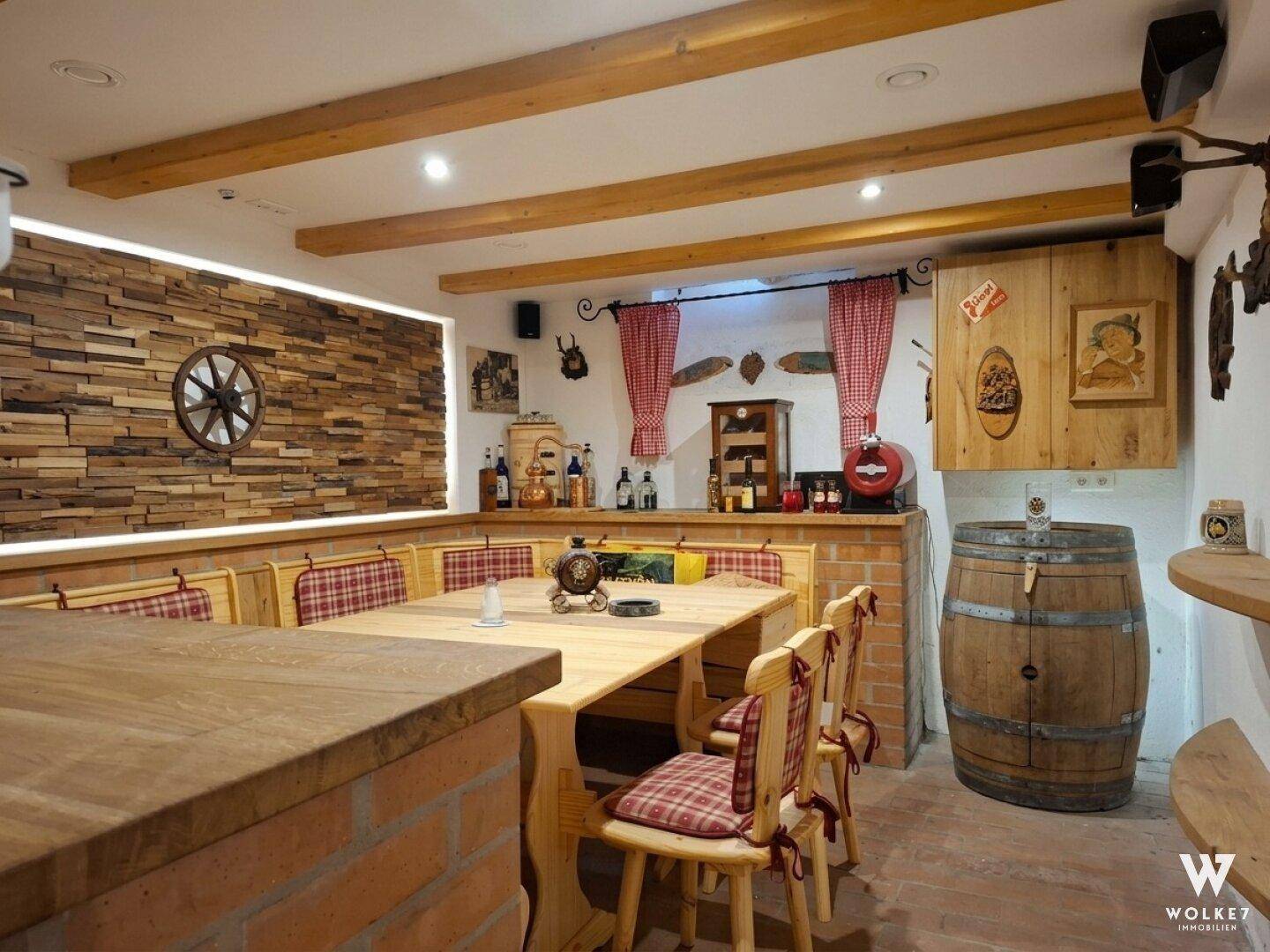 Rustikaler Partyraum im Keller mit Holzbalken, Sitzbänken und einer traditionellen Bar.