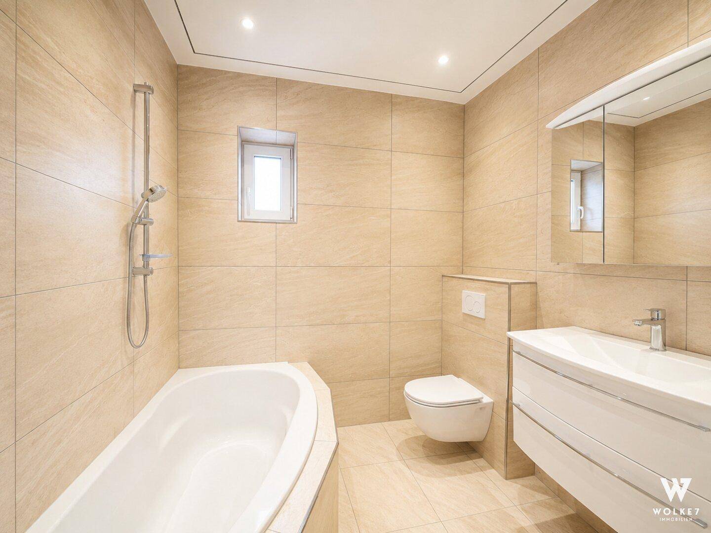 Modernes Badezimmer mit beigefarbenen Fliesen, Badewanne, wandhängendem WC und Fenster.