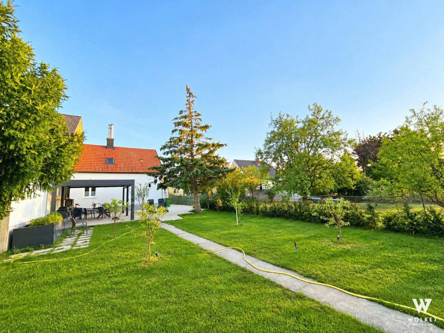 Großer, gepflegter Garten mit Rasenfläche, Bäumen und einem Weg, der zur Terrasse führt.