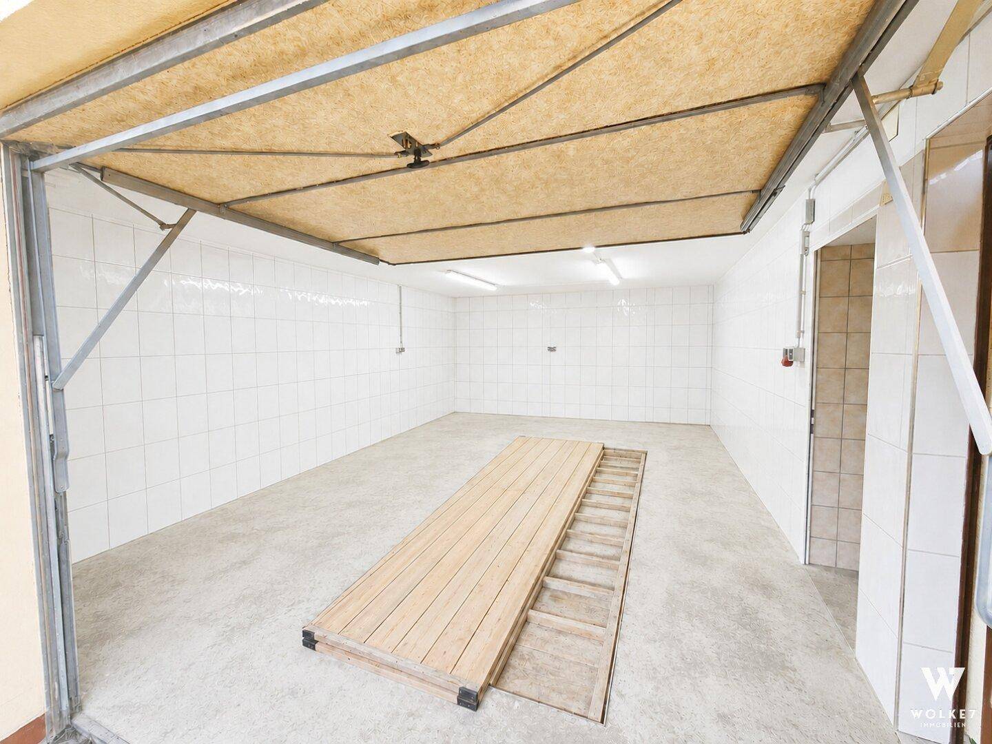Geräumige, geflieste Garage mit Betonboden und einem hölzernen Grubenabdeckung.