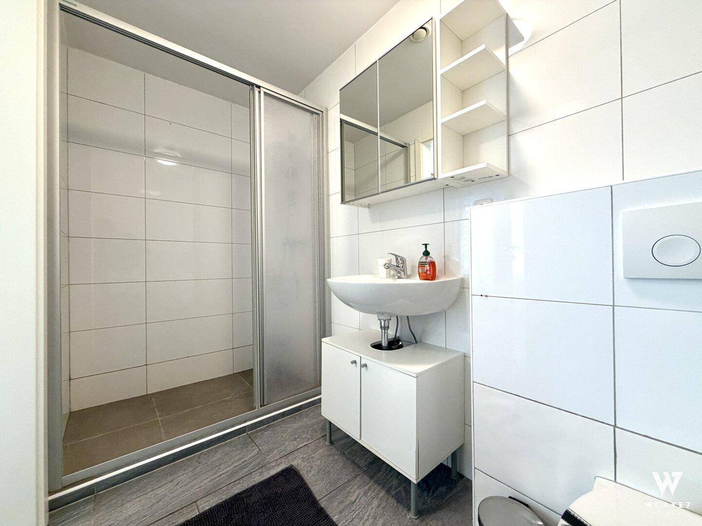 Helles Badezimmer mit weiß gefliesten Wänden, Dusche und modernem Waschtisch.