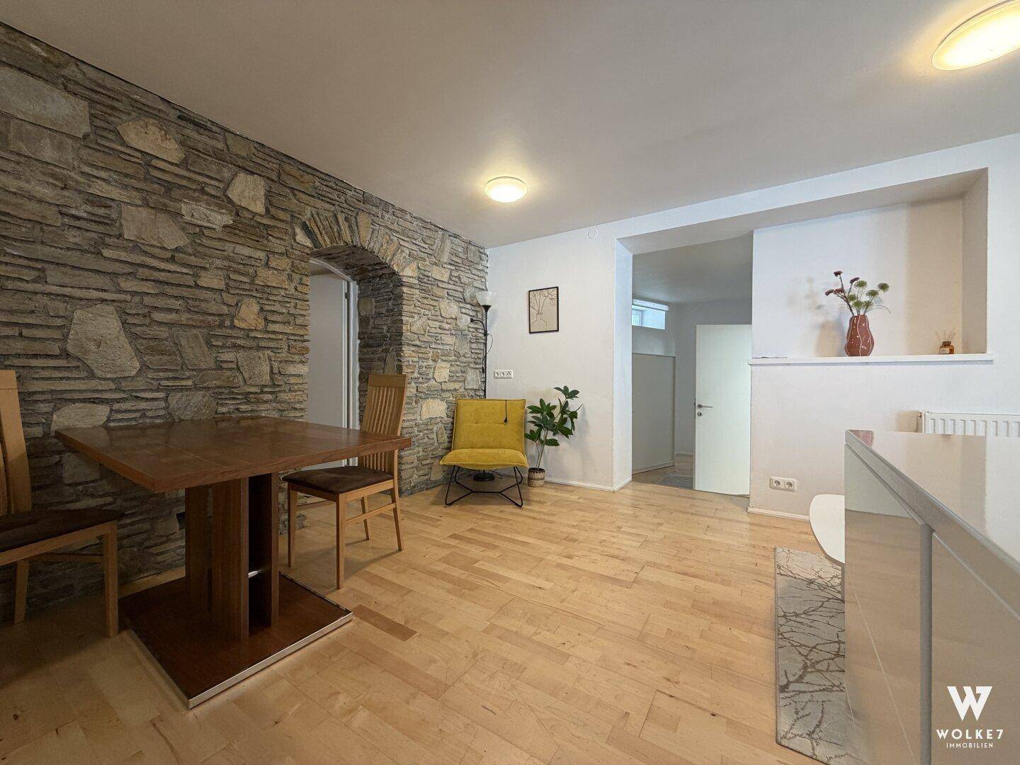 Essbereich mit Holztisch, Stühlen und einer markanten Natursteinwand mit Rundbogen.