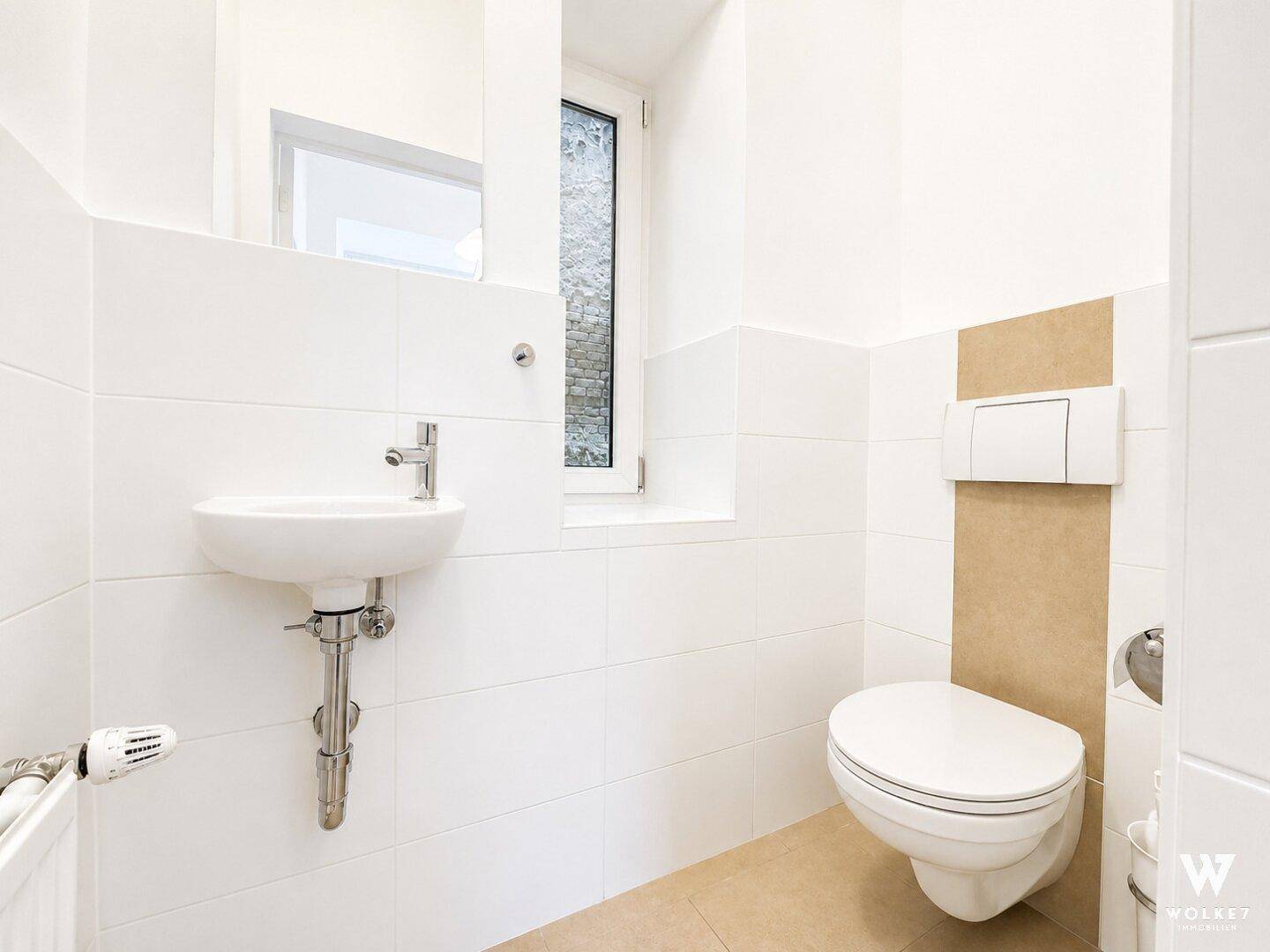 Helles Gäste-WC mit wandhängender Toilette, kleinem Waschbecken und Fenster.