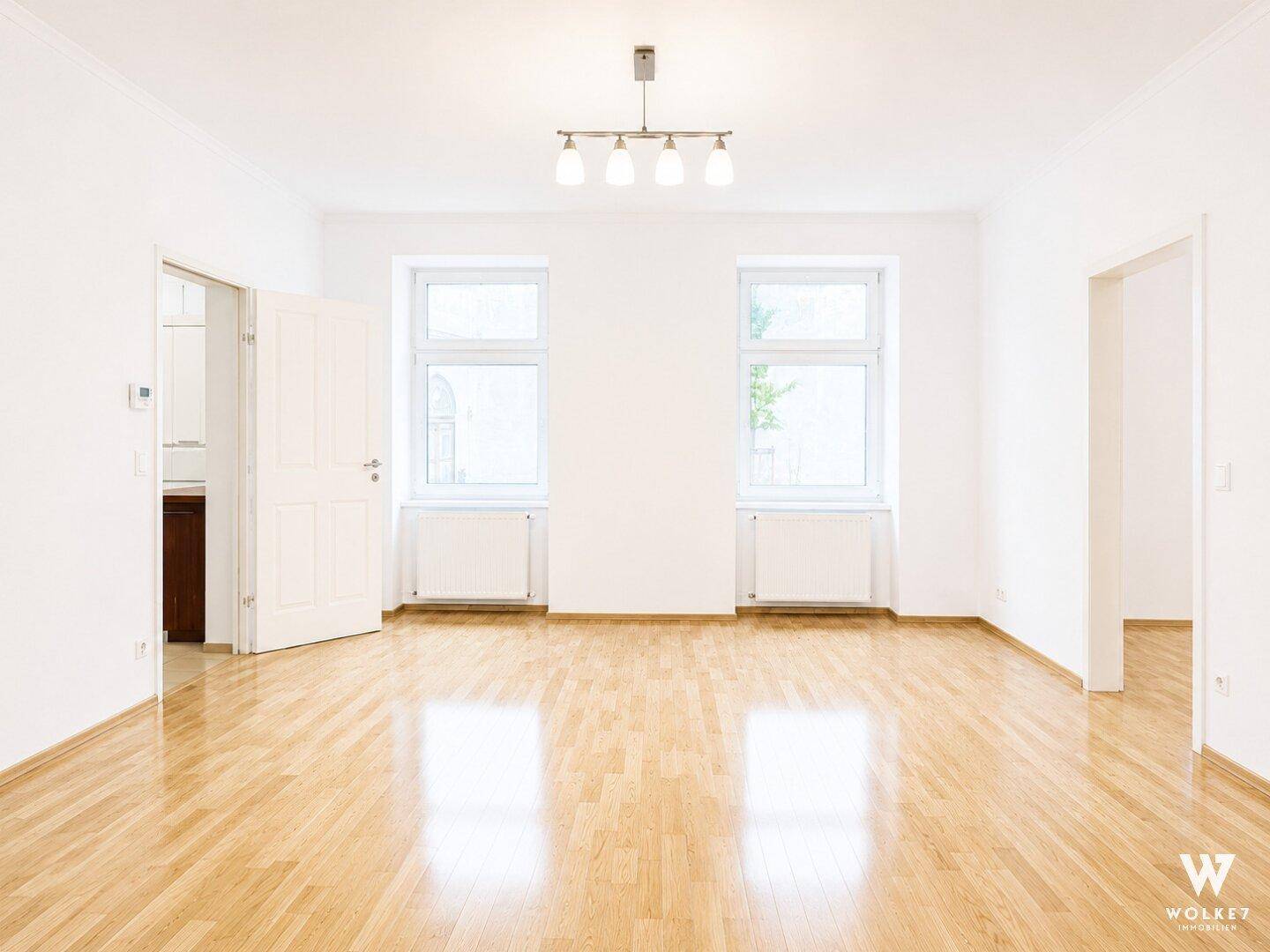 Geräumiges, leeres Wohnzimmer mit hellem Parkettboden und viel Tageslicht.