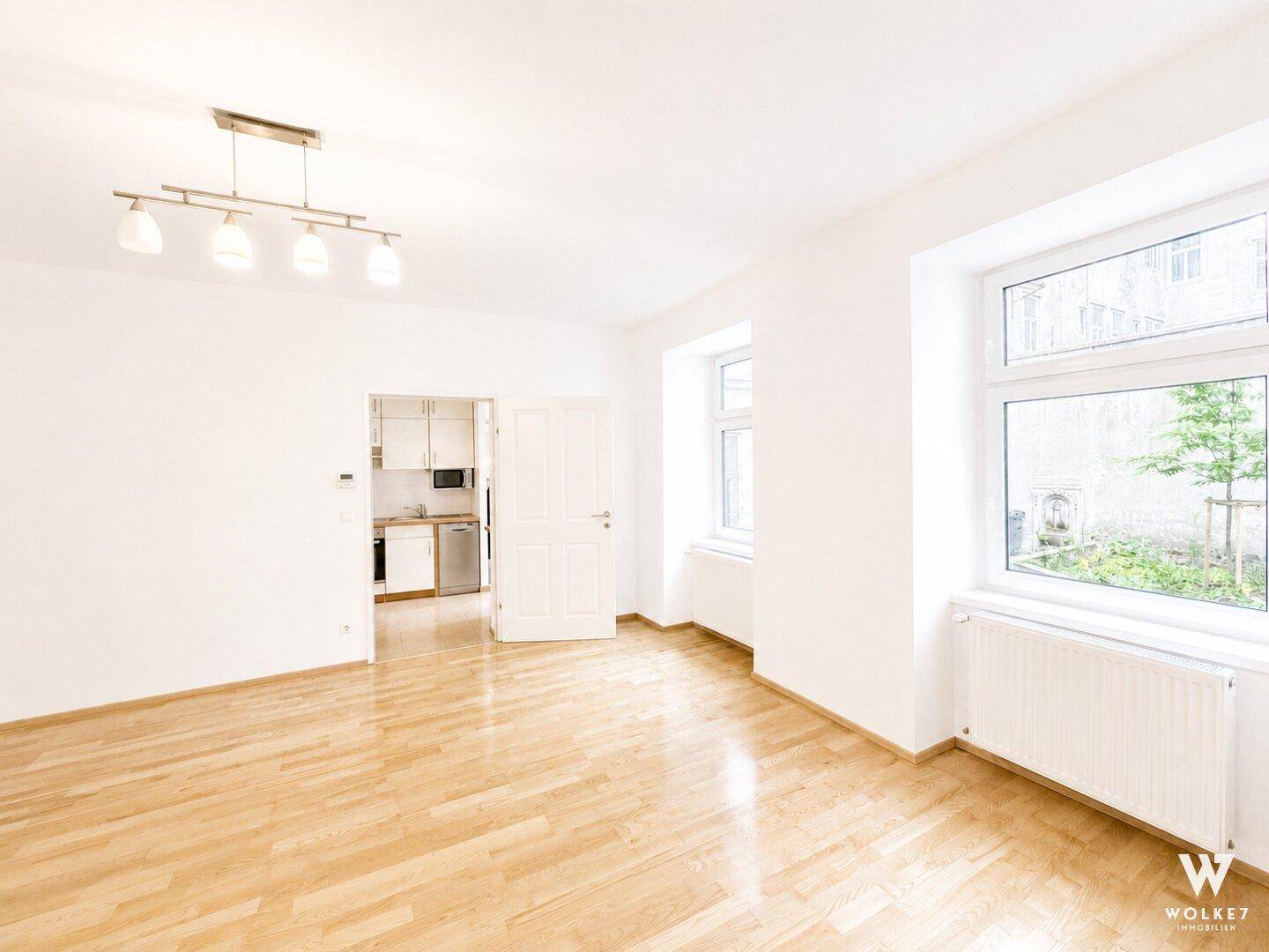 Helles Wohnzimmer mit Parkettboden und Blick in die angrenzende Küche.