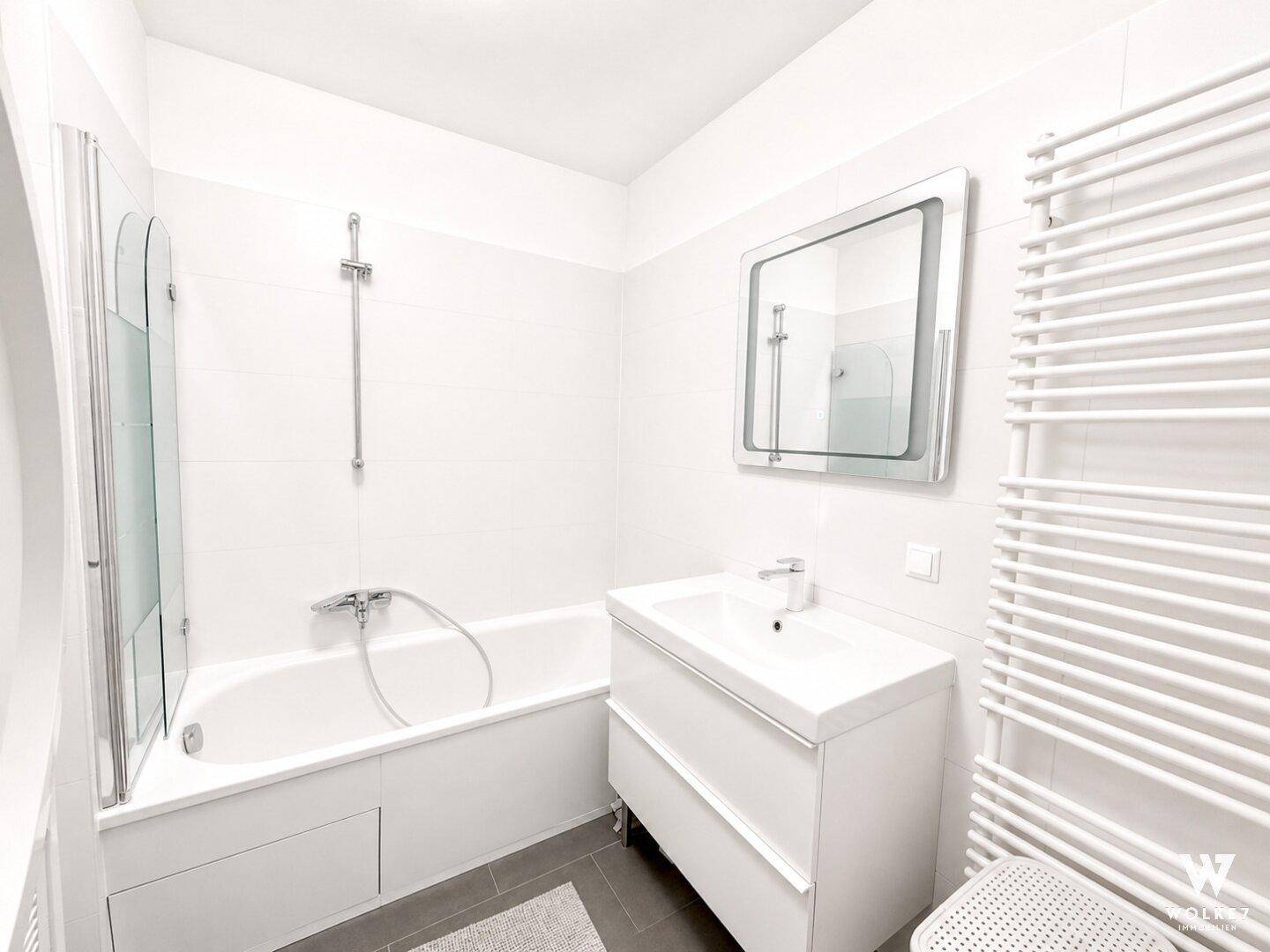 Modernes Badezimmer mit Badewanne, Duschabtrennung und beheiztem Handtuchhalter.