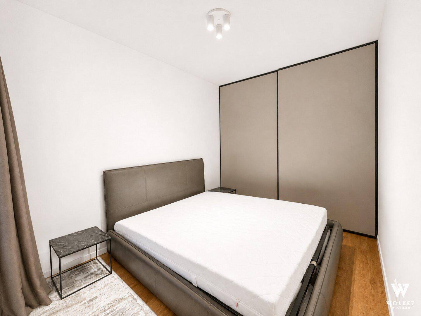 Schlafzimmer mit modernem Bett, Nachttisch und integriertem Kleiderschrank.
