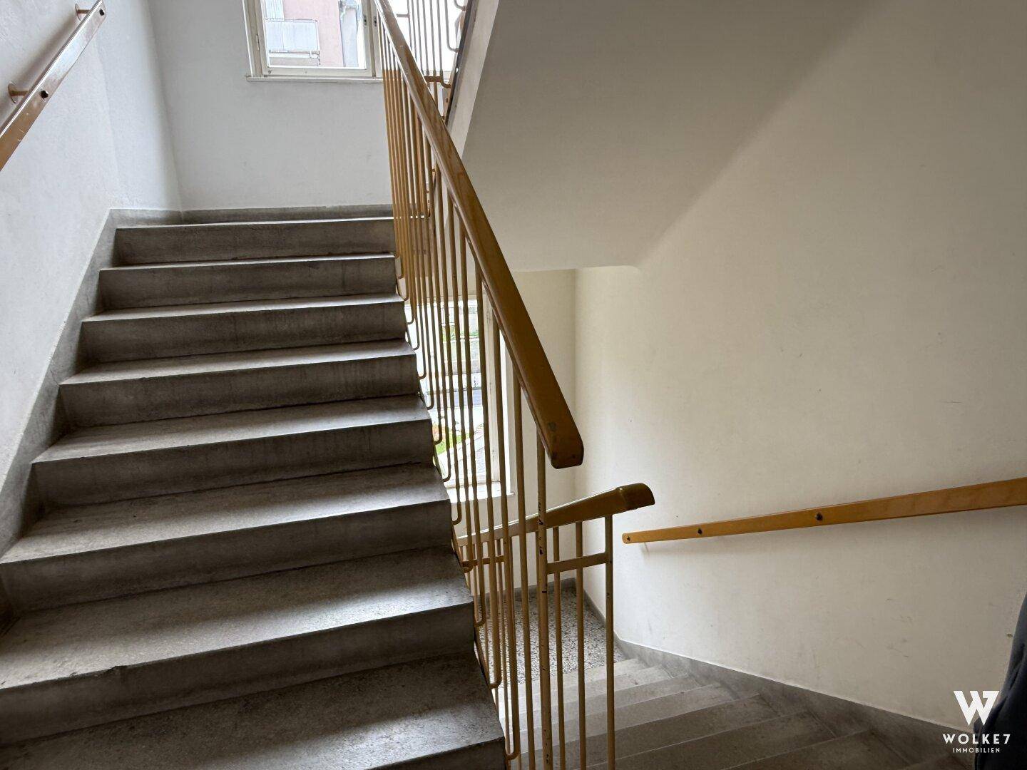 Treppenhaus mit Steinstufen und Holzgeländer in einem Mehrfamilienhaus.