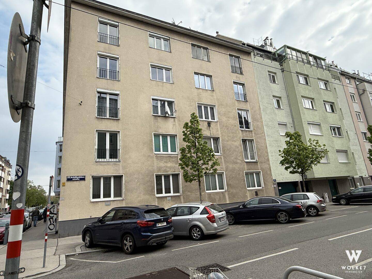 Mehrfamilienhausfassade an einer Straße mit parkenden Autos.