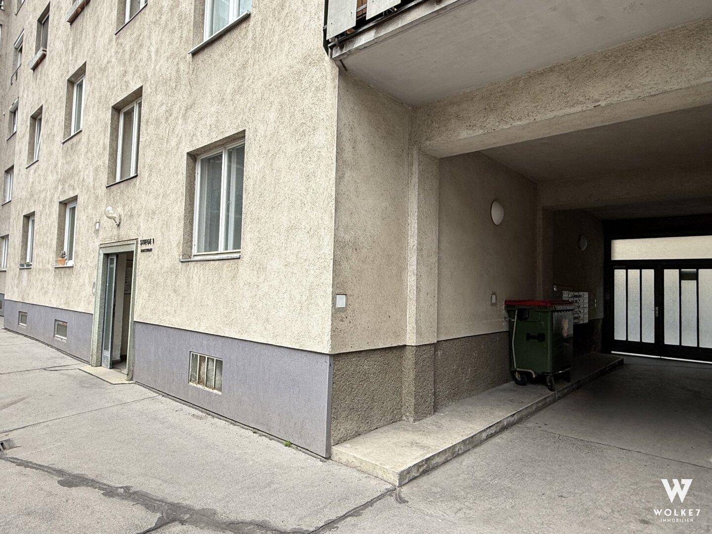 Gebäudeeingang mit Zufahrt und Mülltonnen im Außenbereich.